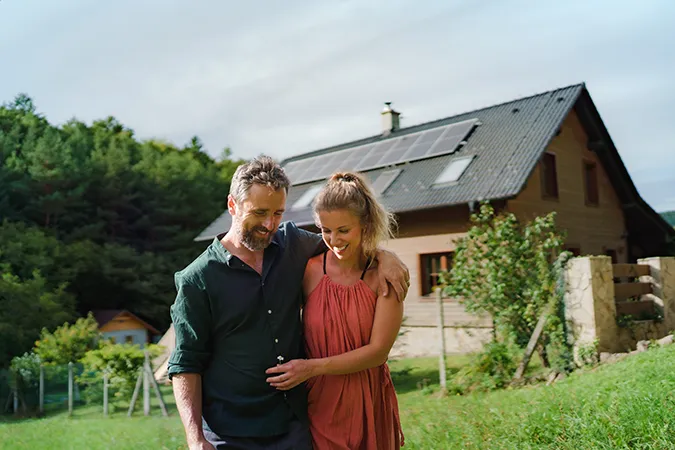 Szczęśliwe małżeństwo przed domem z zamontowaną fotowoltaiką na dachu